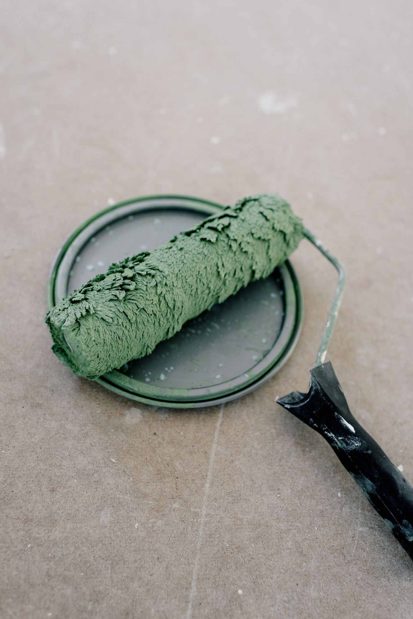 Roller loaded with deep green paint resting on a tin lid
